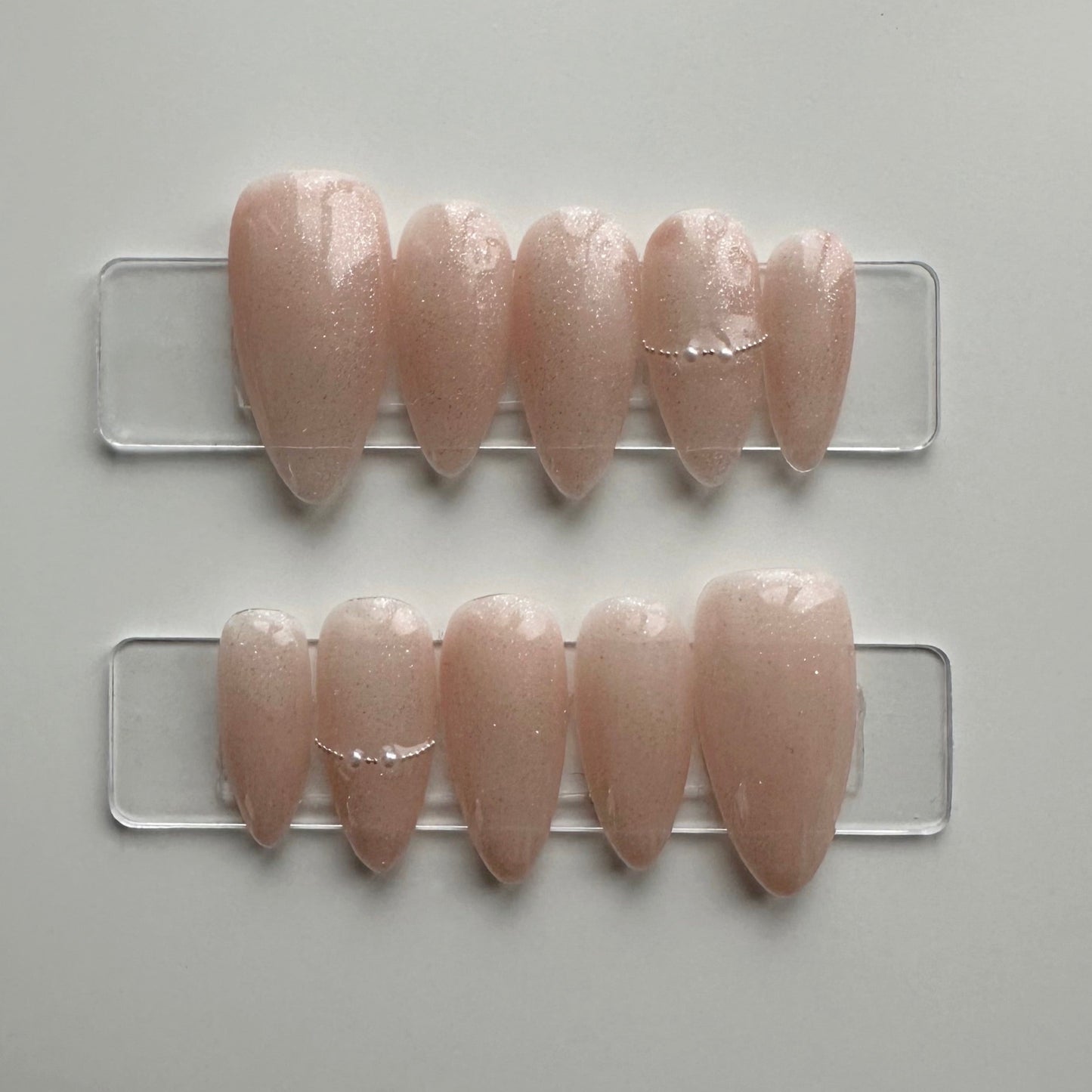 A press-on nail set that feature a nude base with a sparkly coat. it is elegant and simple, perfect for any occasion